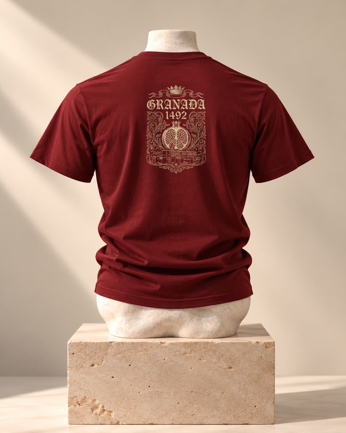 Camiseta Granada 1492 en burdeos, vista de espaldas, sobre un busto de piedra y un pedestal de travertino