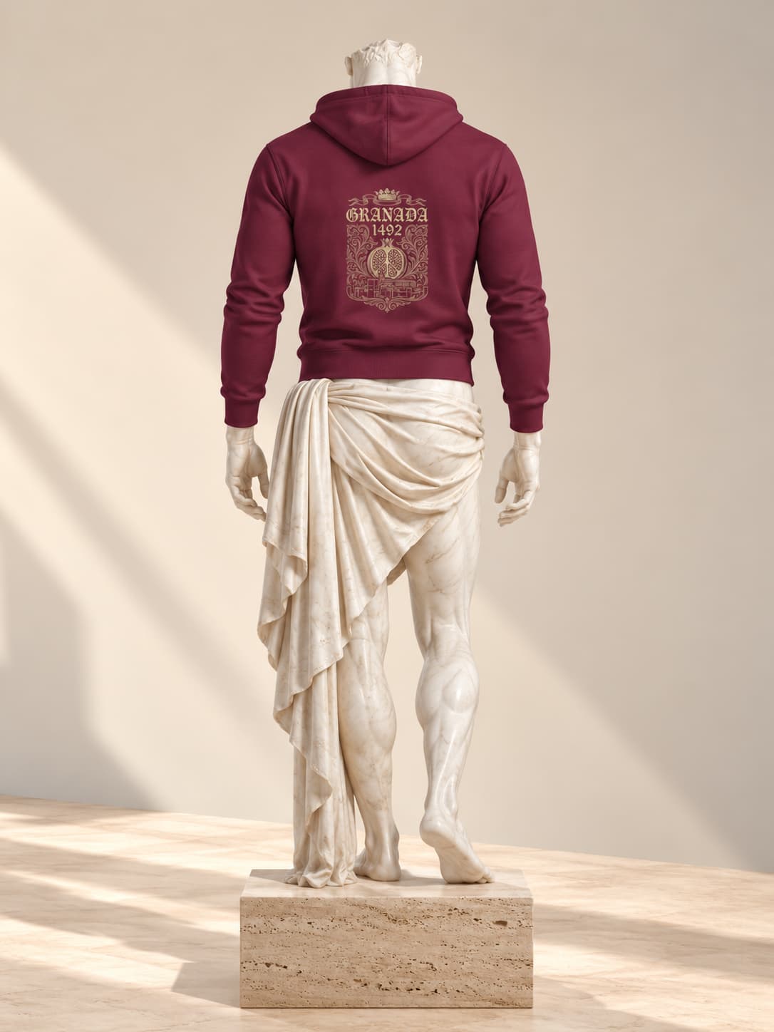 Sudadera Granada 1492 en granate, vista de espaldas, sobre una escultura clásica de mármol, con una cartela ornamentada con una granada abierta, la corona real y «Granada» y «1492» en dorado